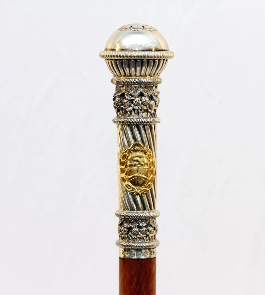 Detalle del bastón presidencial argentino de Raúl Alfonsín, réplica con empuñadura de plata y escudo nacional dorado.