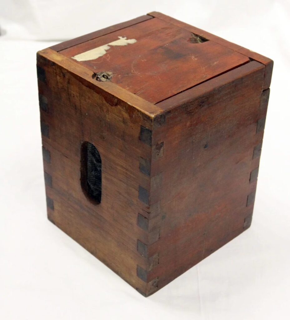 Caja de madera antigua con ranura superior y ensambles tipo cola de milano, utilizada como urna de votación.